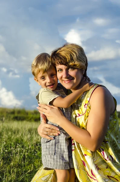 Retrato de mamá feliz besar y sacudir hijo en el jardín de verano verde. Linda madre abrazando bebé niño mirando a la cámara — Foto de Stock