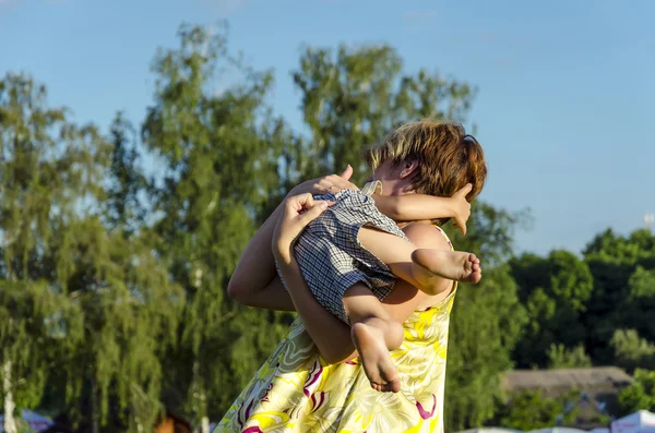 Retrato de feliz pequena mãe beijando e sacudir filho ao ar livre no jardim de verão verde . — Fotografia de Stock