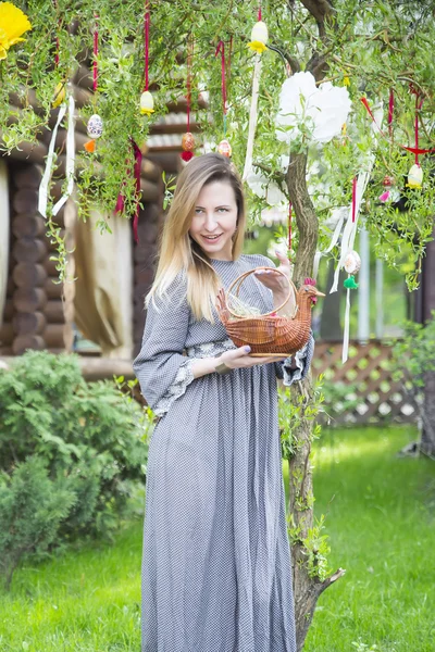 Krásná mladá dívka s košíkem s velikonoční vejce na pozadí velikonoční strom — Stock fotografie