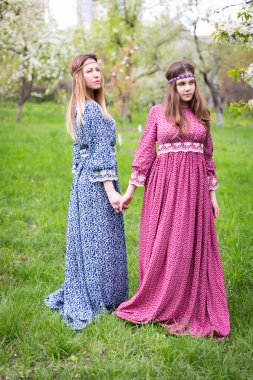 İki güzel kadınlar uzun elbiseler - anne ve kızı yemyeşil bahar bahçe içinde yürüyor