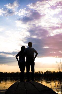 Gün batımında göl kıyısında köprüde çift ayakta