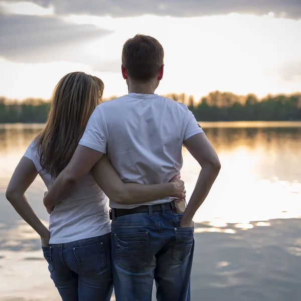 Pareja de pie en el puente en la orilla del lago al atardecer — Foto de Stock