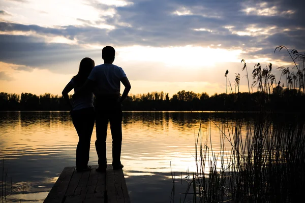 Paar steht bei Sonnenuntergang auf der Brücke am Ufer des Sees — Stockfoto