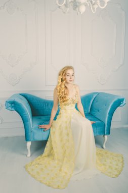 Kanepede uzun altın elbiseli güzel bir genç sarışın tam uzunlukta portresi. Stüdyo. Yüksek moda. Duygular