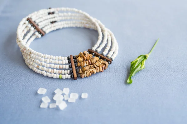 Bianco e collana di perle di pietra di tigre su sfondo blu con zucchero raffinato e pianta — Foto Stock