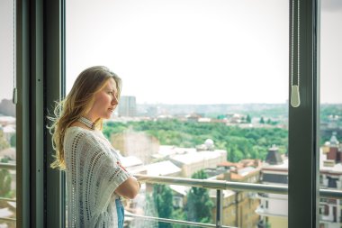 Genç güzel sarışın kız pencereden ayakta ve üzgün