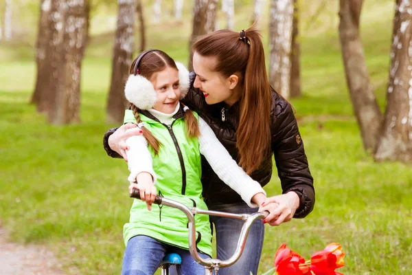 Feliz madre enseña a su hija a montar en bicicleta. Madre apoya positivamente a su hija aprendiendo a andar en bicicleta — Foto de Stock