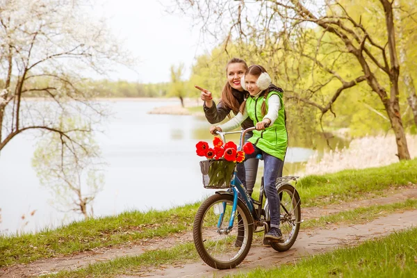 Feliz madre enseña a su hija a montar en bicicleta. Madre apoya positivamente a su hija aprendiendo a andar en bicicleta — Foto de Stock