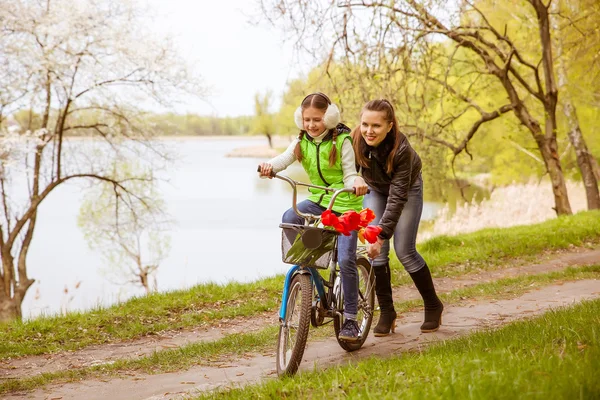 Szczęśliwa matka uczy córkę do jazdy na rowerze. Matka posiada córka od upadku — Zdjęcie stockowe