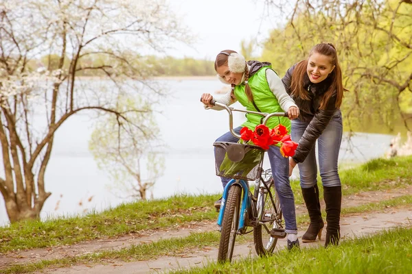 Szczęśliwa matka uczy córkę do jazdy na rowerze. Matka posiada córka od upadku — Zdjęcie stockowe