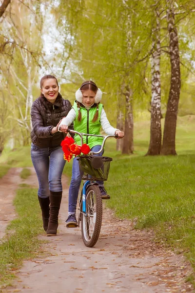 Feliz madre enseña a su hija a montar en bicicleta. Madre sostiene hija de caer — Foto de Stock
