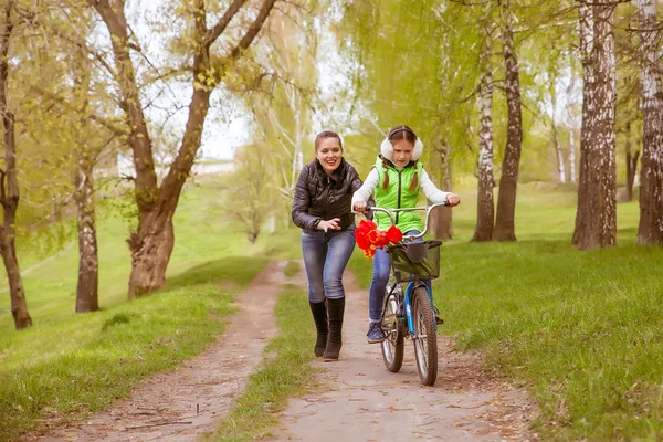 Boldog anya tanítja a lányát, hogy kerékpározni. Anya lánya sikereit örömmel — Stock Fotó