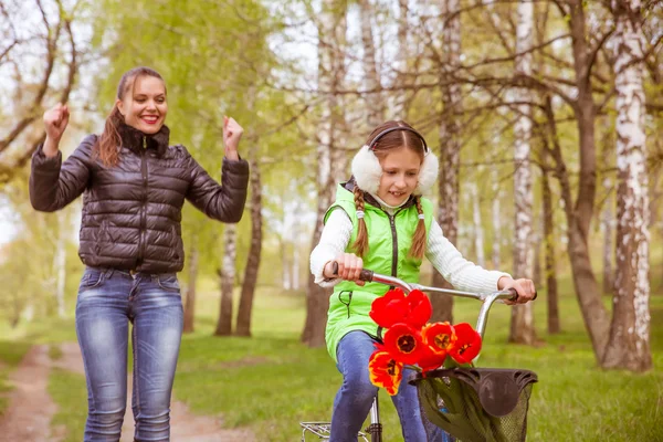 Feliz madre enseña a su hija a montar en bicicleta. Una madre se alegra a los éxitos de la hija — Foto de Stock