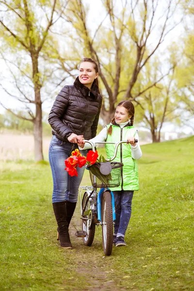 Hija y madre caminan a lo largo de la orilla del lago con una bicicleta y hablan. Valores familiares, educación — Foto de Stock