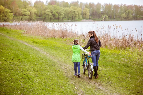 Hija y madre caminan a lo largo de la orilla del lago con una bicicleta y hablan. Valores familiares, educación — Foto de Stock