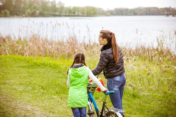 Lánya és anyja séta a parton a tó, a kerékpár, és beszélni. Családi értékek, oktatás — Stock Fotó