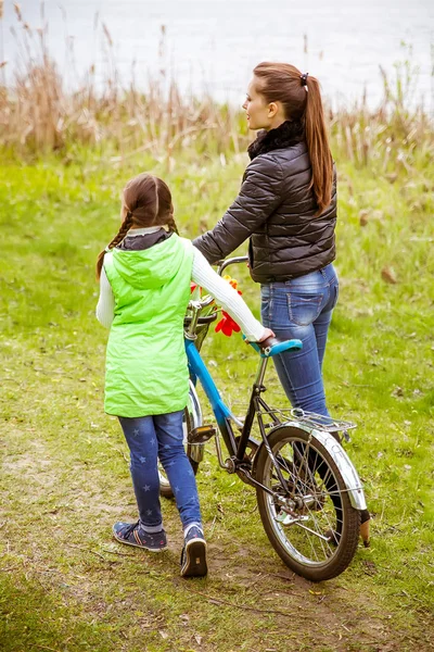 Hija y madre caminan a lo largo de la orilla del lago con una bicicleta y hablan. Valores familiares, educación — Foto de Stock