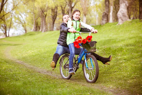 La hija lleva a su madre en una bicicleta en el lago en el parque. Se están divirtiendo. . — Foto de Stock