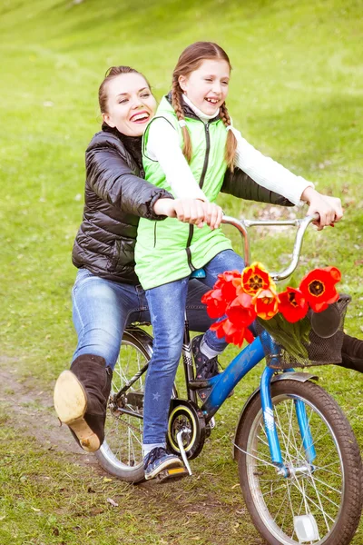 La hija lleva a su madre en una bicicleta en el lago en el parque. Se están divirtiendo. . — Foto de Stock