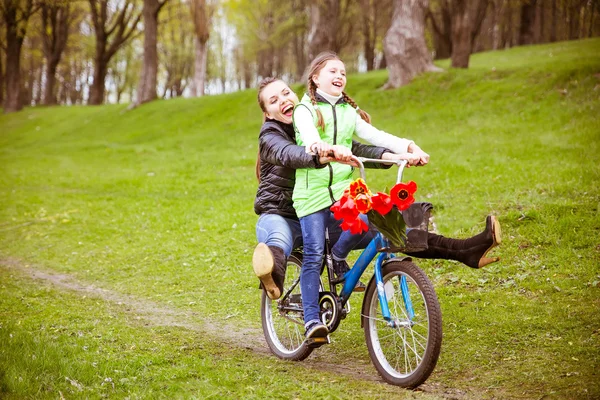 La hija lleva a su madre en una bicicleta en el lago en el parque. Se están divirtiendo. . — Foto de Stock