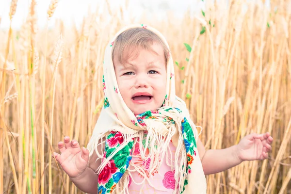 Das kleine Mädchen mit Schal steht mitten auf dem Feld und weint. Waisenkinder, soziale Probleme. — Stockfoto