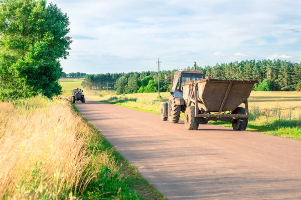 Twee trekkers de onverharde weg richting tijdens de oogst op het gebied — Stockfoto