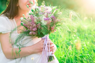 Alanları ve ormanların bir arka plan üzerinde beyaz elbiseli genç gelinin elinde bir buket closeup