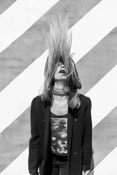 Όμορφη μόδας νεαρή γυναίκα είναι στέκεται κοντά στον τοίχο ριγέ και τινάζει τα μαλλιά της — Φωτογραφία Αρχείου