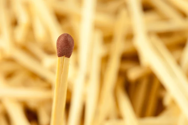 Single matchstick on blurred background of wooden sticks — Stock Photo, Image