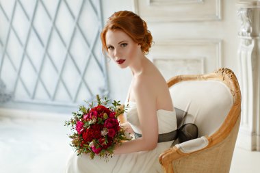 Very pretty sophisticated red-haired girl sitting in a chair wit