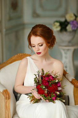 Very pretty sophisticated red-haired girl sitting in a chair wit