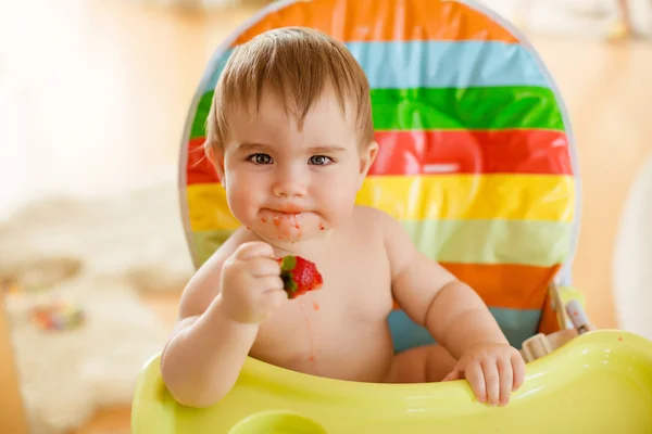 Pequeño niño sentado en una silla brillante, comiendo fresas — Foto de Stock