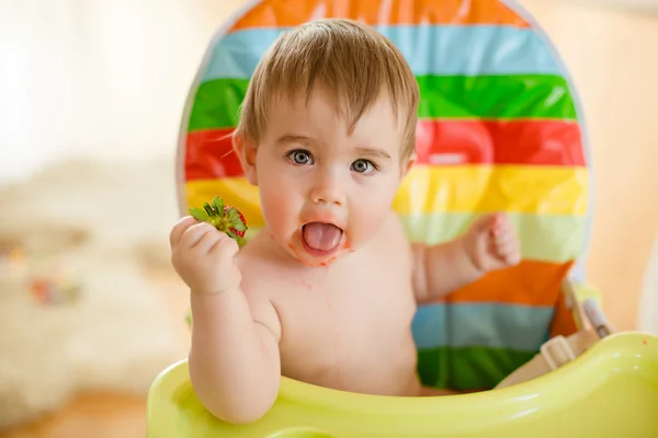 Baba kisfiú ül egy fényes széken, eszik szamóca — Stock Fotó