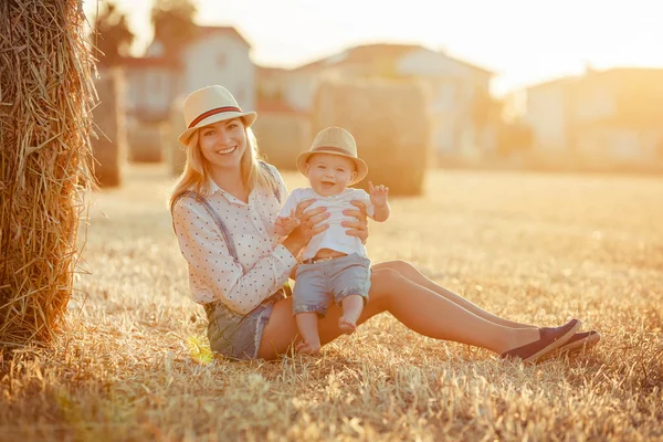 A young mother with  little baby boy in cap sitting on a backgro — Stock Photo, Image