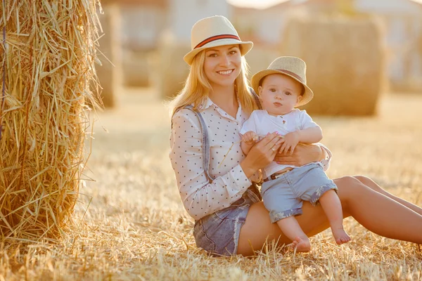 Una madre joven con un niño pequeño en gorra sentado en un backgro —  Fotos de Stock