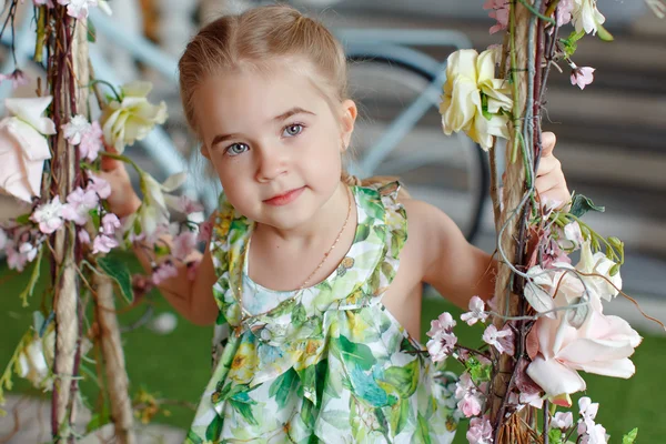 Niedliches kleines Mädchen in einem grünen Kleid sitzt auf Schaukeln dekoriert wi — Stockfoto