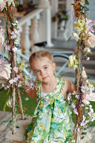 Menina bonito em um vestido verde sentado em balanços decorados wi — Fotografia de Stock