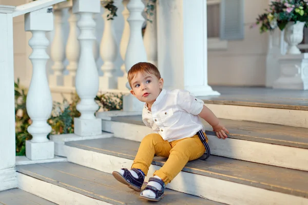 Kleine heel schattig, charmante jongen in gele broek zit op de sta — Stockfoto