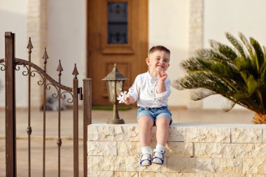 Beyaz gömlekli küçük bir erkek bebek arka planda oturuyor. 