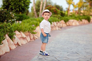 Bir park arka plan üzerinde yaz şapka ve şort küçük çocuk yürümeye başlayan