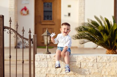 Beyaz gömlekli küçük bir erkek bebek arka planda oturuyor. 