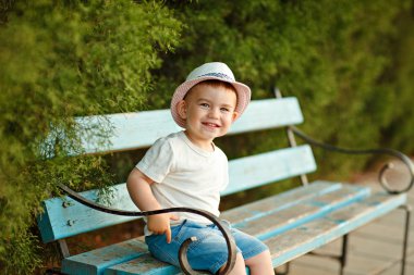 Bir bankta oturan ve s gülümseyen bir şapka küçük bebek çocuk