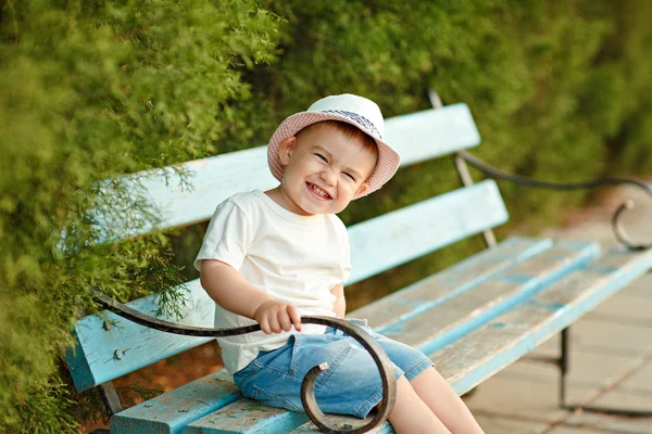 Pequeño niño en un sombrero sentado en un banco en el verano y ch — Foto de Stock