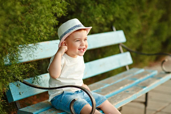 Little Baby Boy w kapeluszu siedzi na ławce w lecie i ch — Zdjęcie stockowe