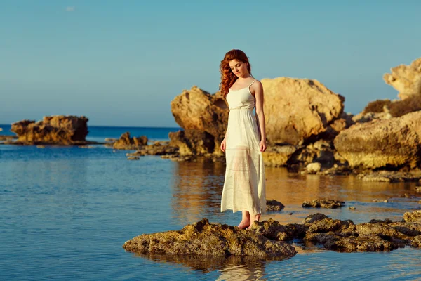 La fille sensuelle aux cheveux roux dans une robe blanche debout sur la mer — Photo