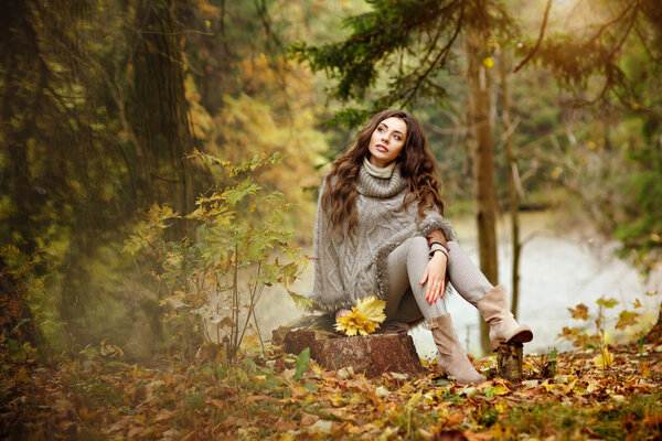 Portrait of a beautiful, dreamy and sad girl with long wavy hair to knit a sweater, in full growth, the fall in the park