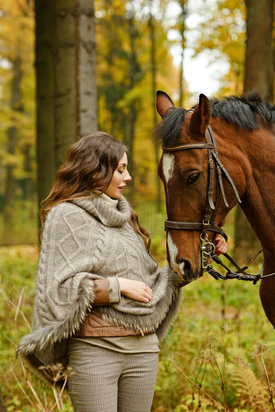 Retrato de uma menina com cabelos longos alimentando um cavalo em um parque no outono — Fotografia de Stock