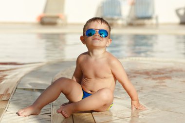 Gözlüklü küçük sevimli tombul erkek bebek arka bir havuzda oturan