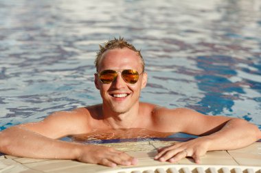 Young handsome blond man in sunglasses in the pool emotionally l
