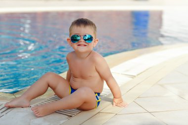 Gözlüklü küçük sevimli tombul erkek bebek arka bir havuzda oturan